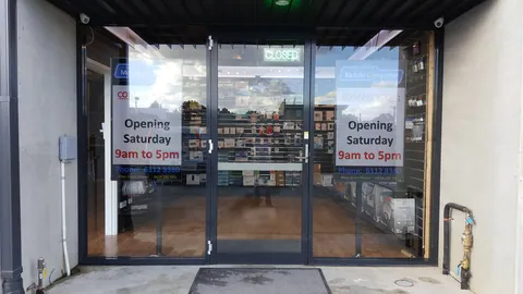 The shopfront in daylight with its signs and Saturday-hours notices.