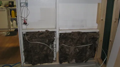 Insulation starts filling the spaces between the wall studs.