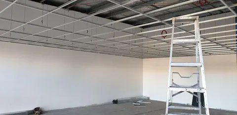Ceiling-grid work progresses above the ladders.