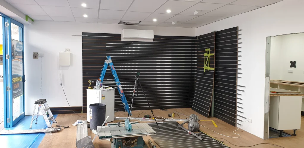 Black slatwall display panels being installed with ladders and tools in the showroom