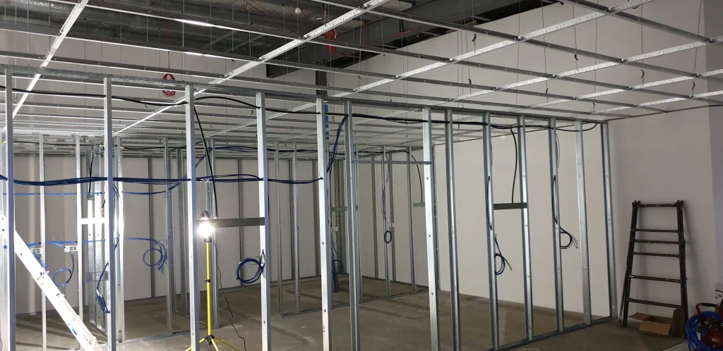 Metal wall studs and ceiling framework with blue cables routed through the new workshop