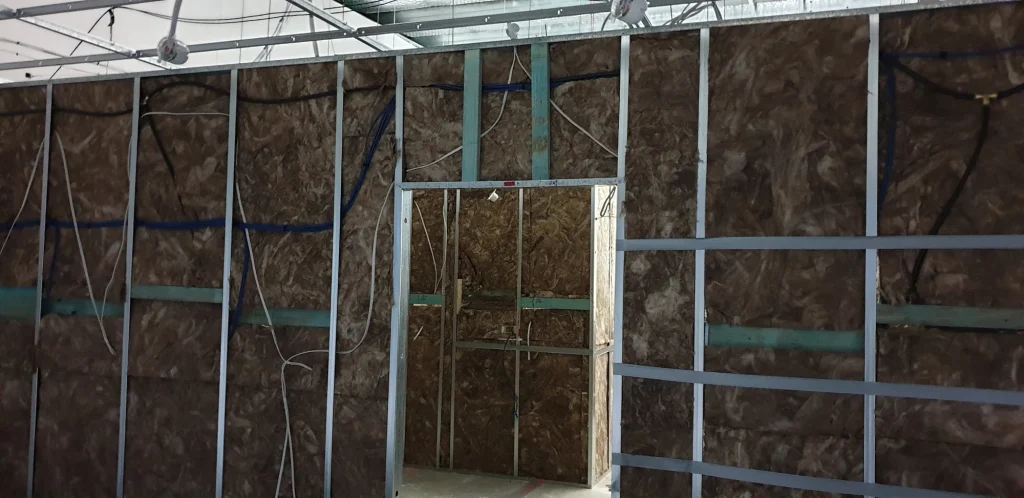 Insulation between metal wall studs with electrical and data cables visible