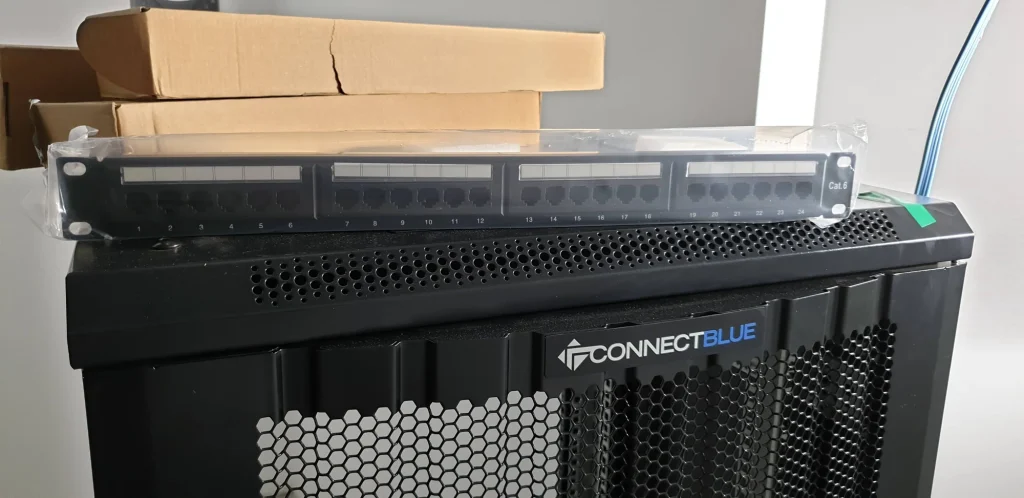 Black network cabinet with a boxed Cat6 patch panel resting on top