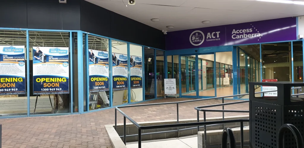 Crawfords opening-soon posters on the blue-framed shopfront beside Access Canberra