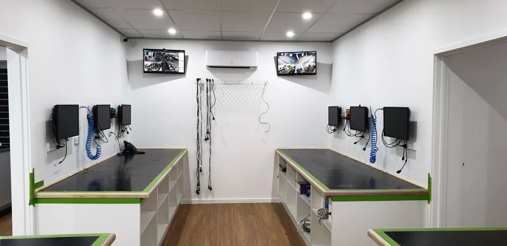 Two rows of new repair benches with wall-mounted monitors, tools, coiled air hoses and overhead screens