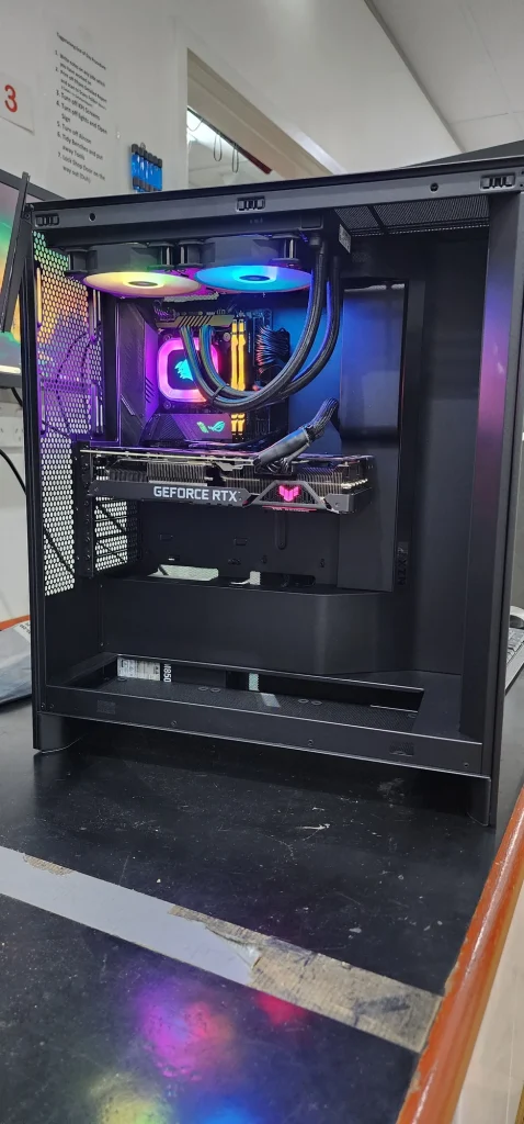 Desktop gaming PC with its side panel removed, showing RGB lighting, liquid-cooling tubes and a GeForce RTX graphics card