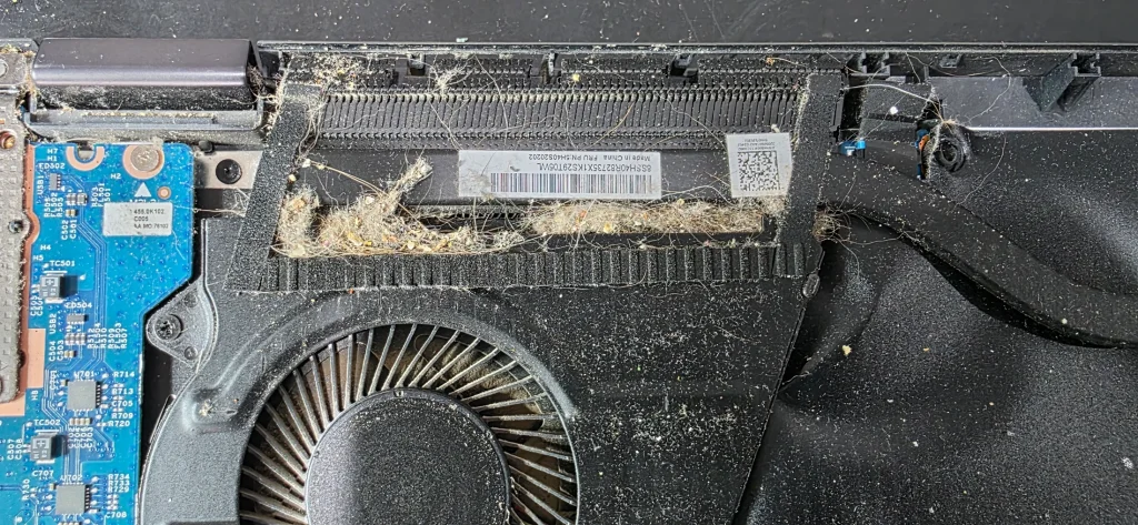 Thick mat of dust and fluff lodged between a laptop cooling fan and the cooling fins, photographed before cleaning