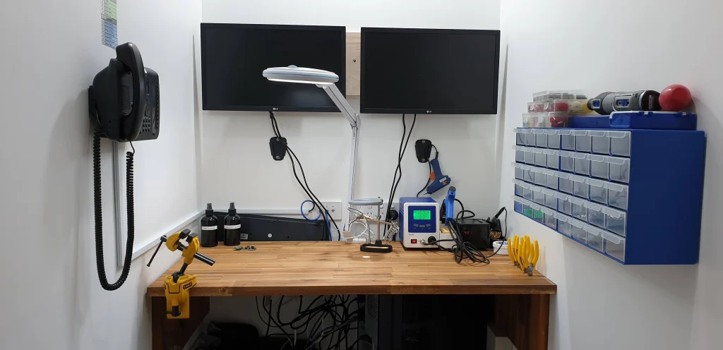 Electronics repair bench with a magnifying lamp, soldering equipment and organised small-parts drawers